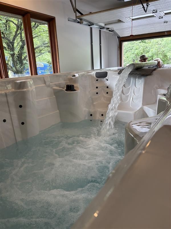 Indoor white swim spa with water flowing, near windows.