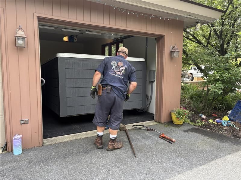 Man installing a large, dark gray hot tub inside a garage.