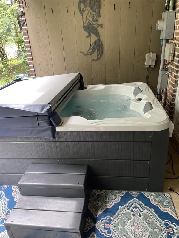 Hot tub with partially open cover on a deck; gray steps; mermaid decor on wall.
