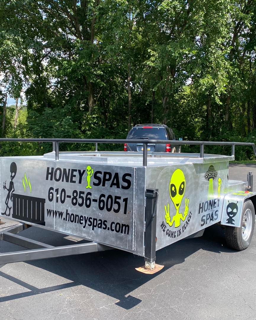 A trailer with a large silver hot tub, decorated with aliens and the text 