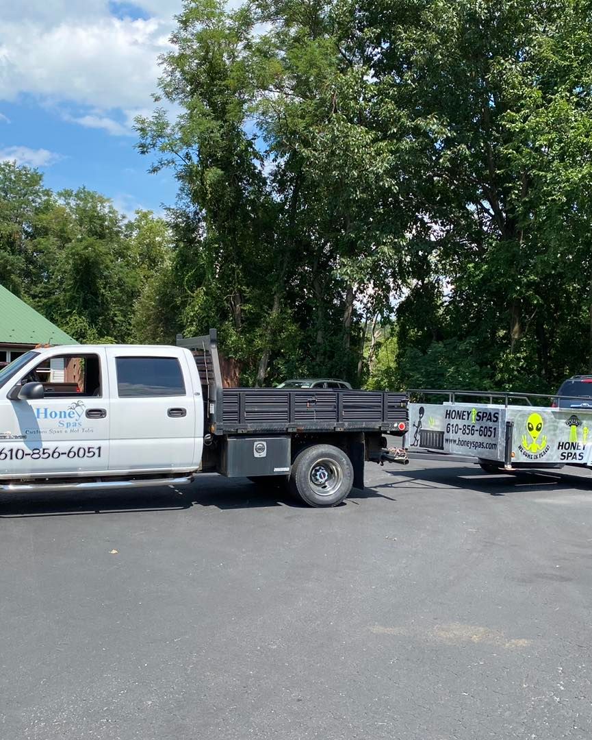 White pickup truck with a flatbed trailer on asphalt, parked in front of a green roofed building.