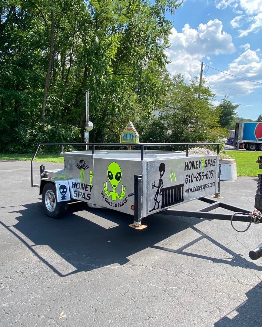 A trailer with alien graffiti, a long antenna, and a sign with a phone number.