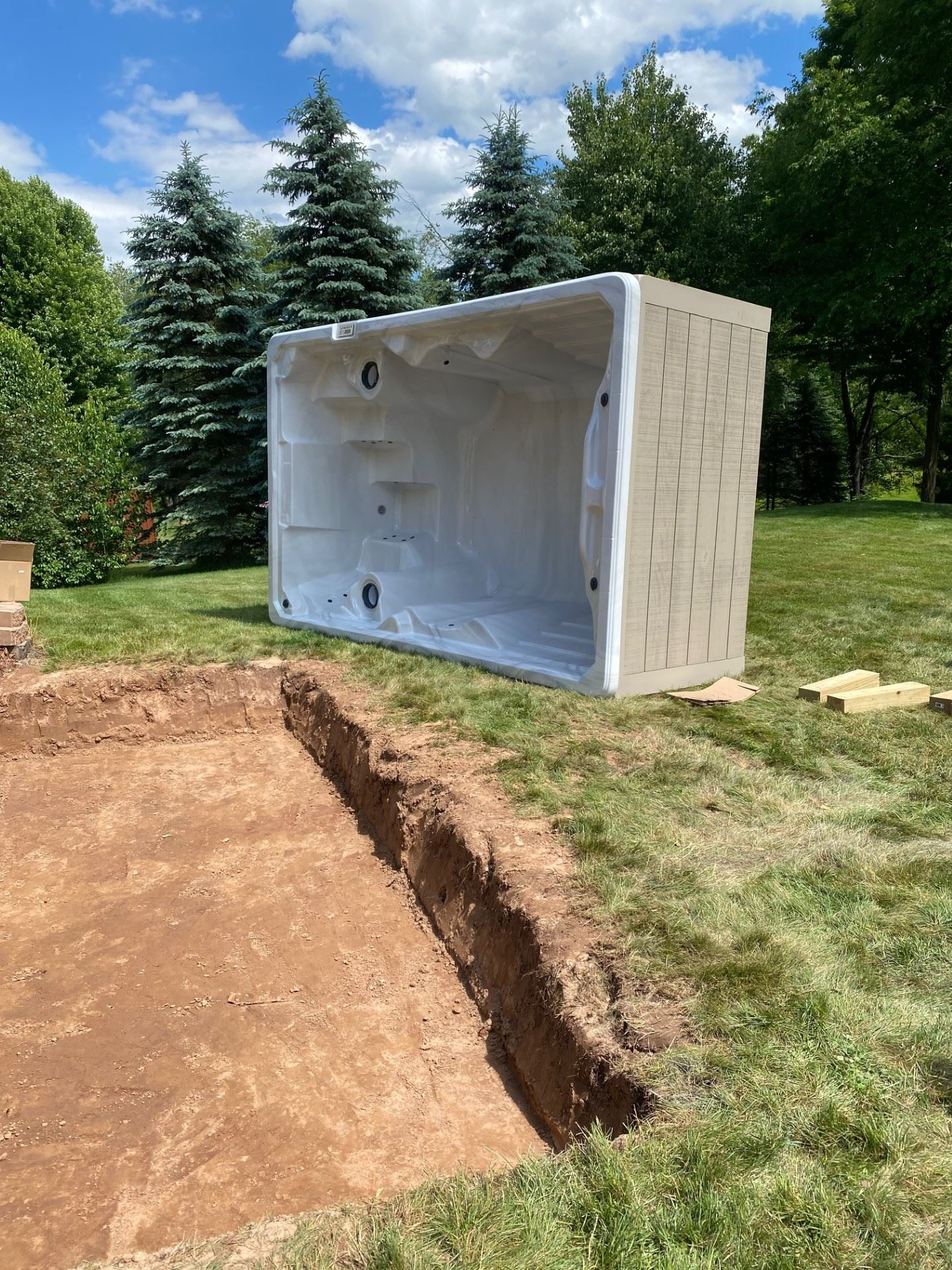 Spa being installed in a backyard; a rectangular pit is dug with the spa adjacent on the grass.