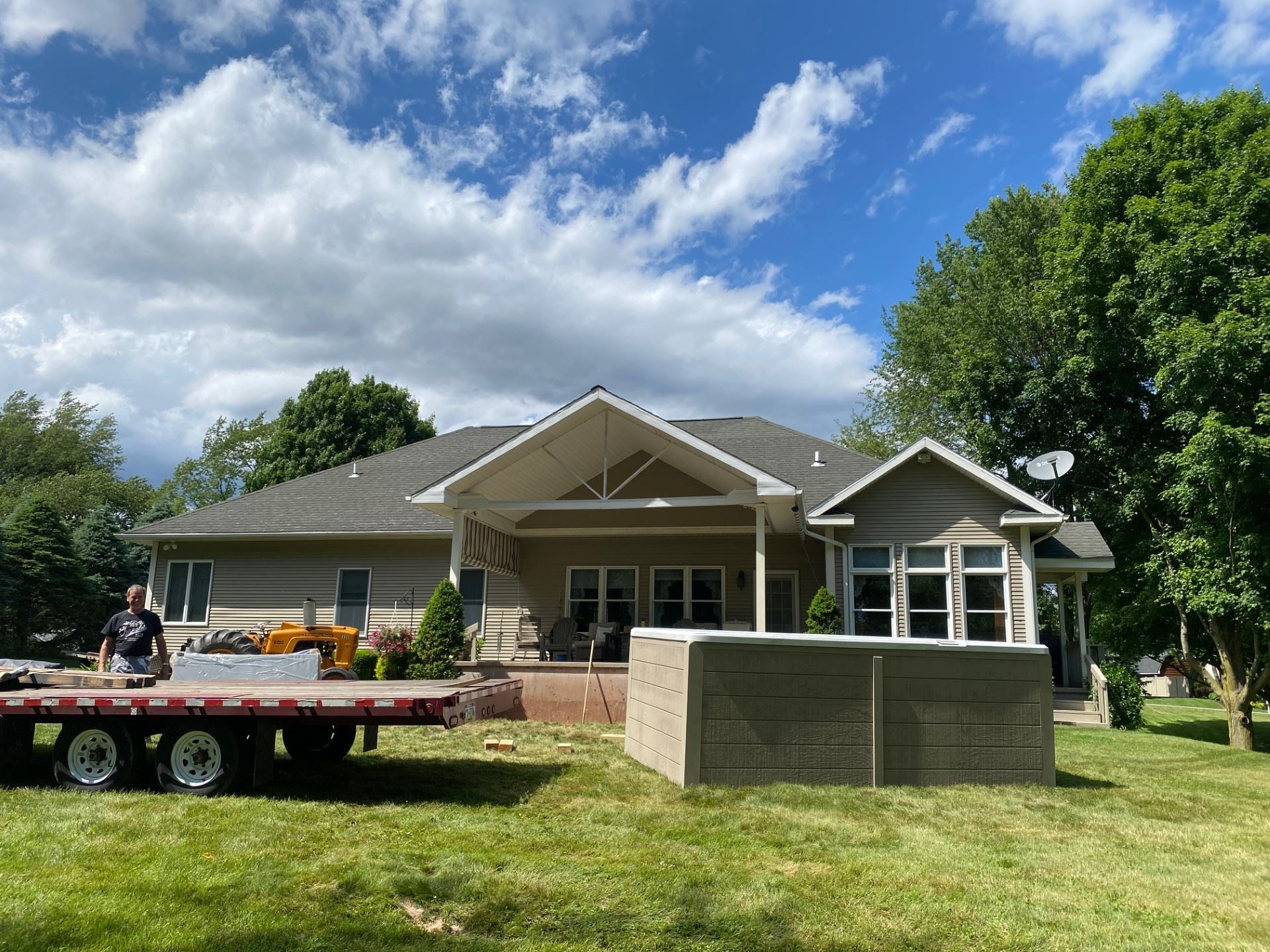 Man near a trailer with equipment, setting up a structure in a backyard with a house on a sunny day.