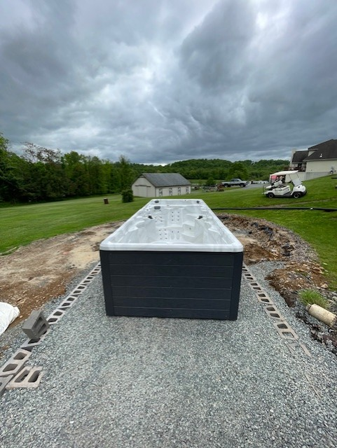 Long rectangular black hot tub on gravel base, set in a grassy yard. Overcast sky.