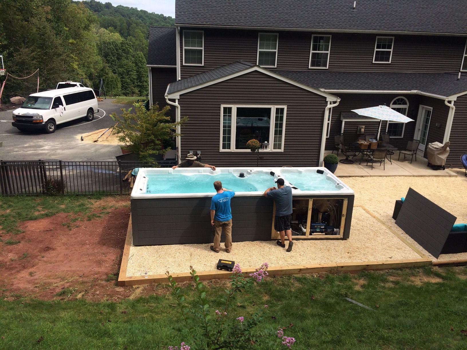 Two men installing a rectangular hot tub in a backyard, near a house and van.