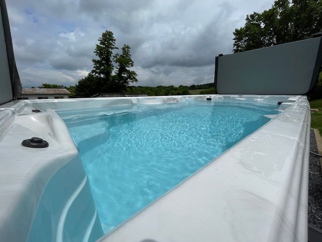 White swim spa filled with blue water under a cloudy sky, in an outdoor setting.