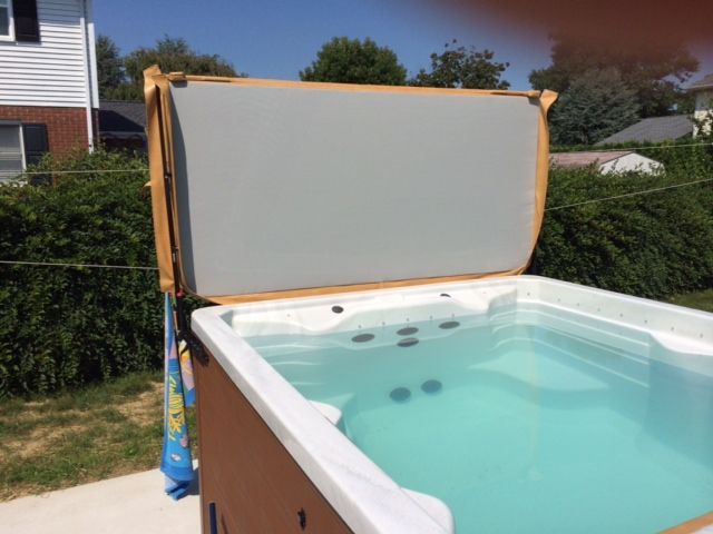 Hot tub with cover raised, filled with blue water, outdoors on a sunny day.