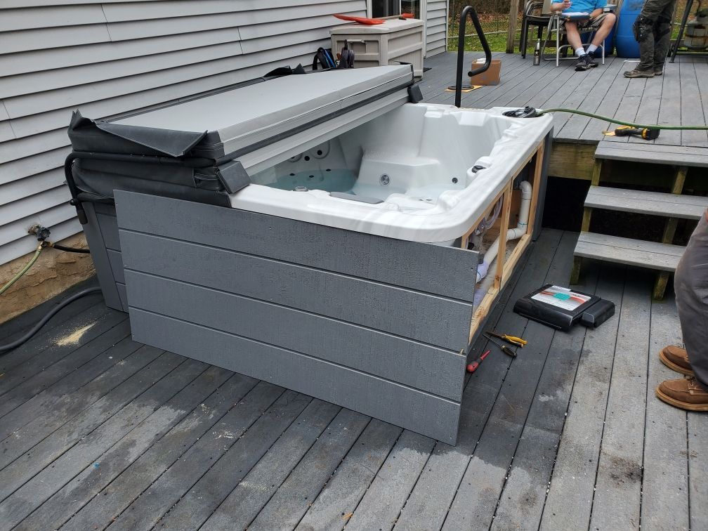 Hot tub on a wooden deck with partially removed gray siding. Deck and house in the background.