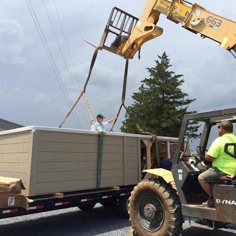 Forklift lifting a hot tub off a trailer. Two men are present at an outdoor construction site.