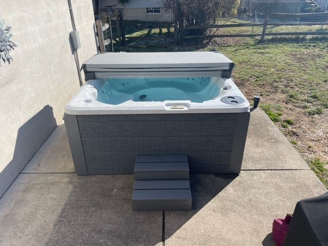A hot tub with the cover partially open on a concrete patio. Steps lead up to the tub.