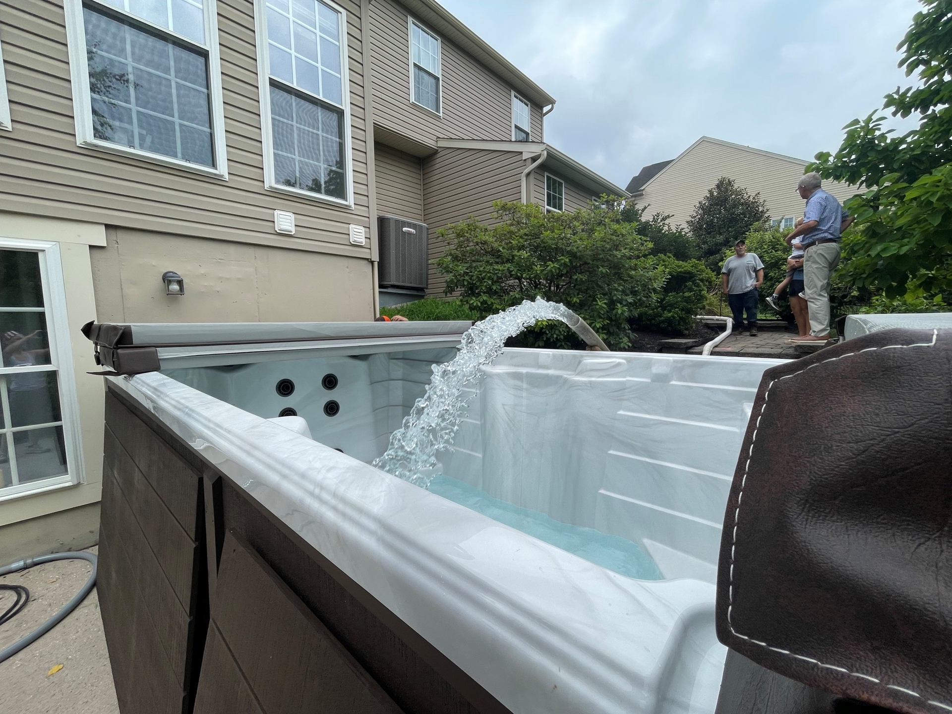 Above-ground pool being filled with water in a backyard, with two people nearby.