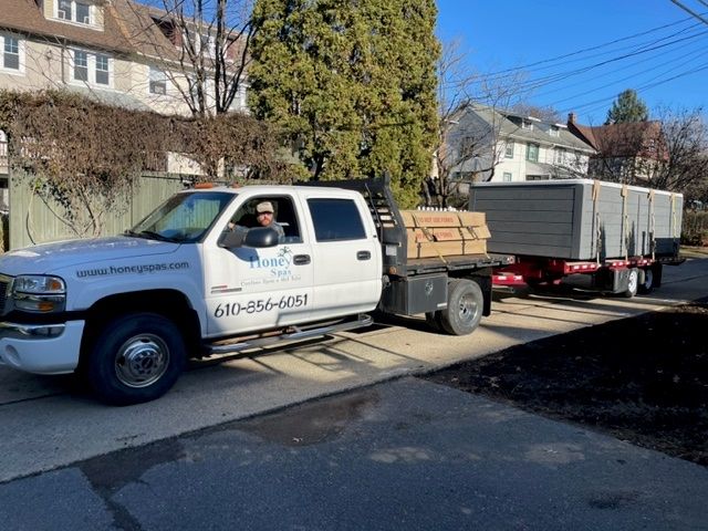 White truck towing a trailer loaded with materials, driver smiling. Residential street.