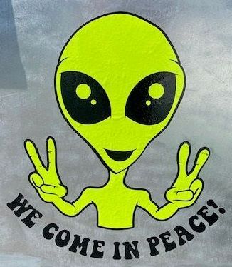 Green alien with large black eyes and peace signs,