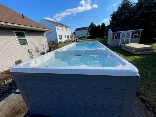Long rectangular swim spa filled with water, in a backyard setting.