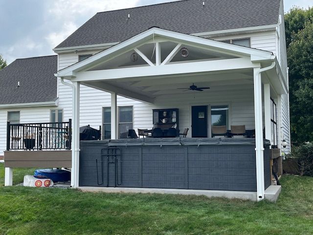 Covered patio with a dark gray hot tub, attached to a white house. Green grass.