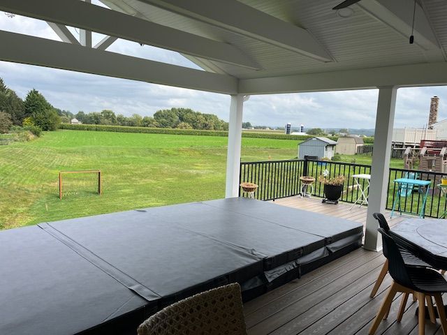 Covered hot tub on deck overlooking green field under overcast sky.
