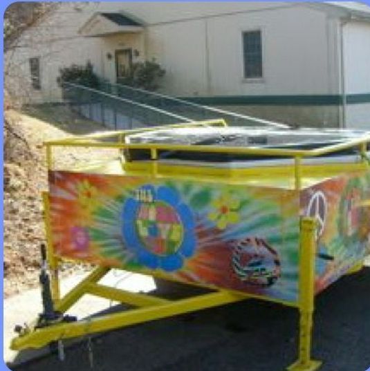 Tie-dye painted trailer with a peace sign parked in front of a light-colored building.