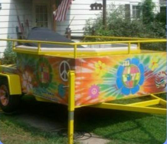 Yellow trailer decorated with tie-dye and peace signs, parked in front of a house.