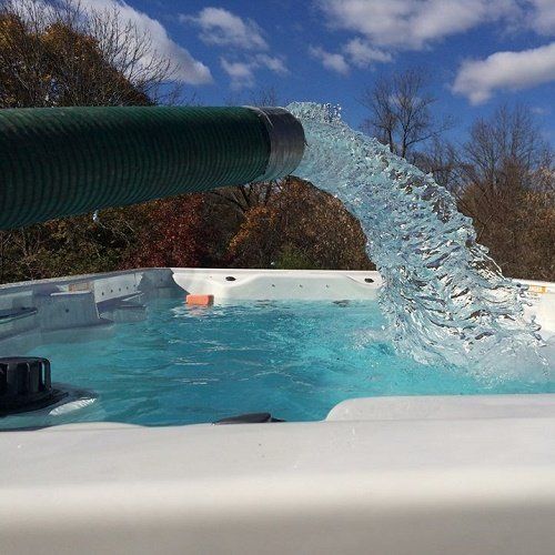 Water pours from a green hose into a white hot tub on a sunny day.