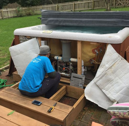 A man is working on a hot tub in a backyard.