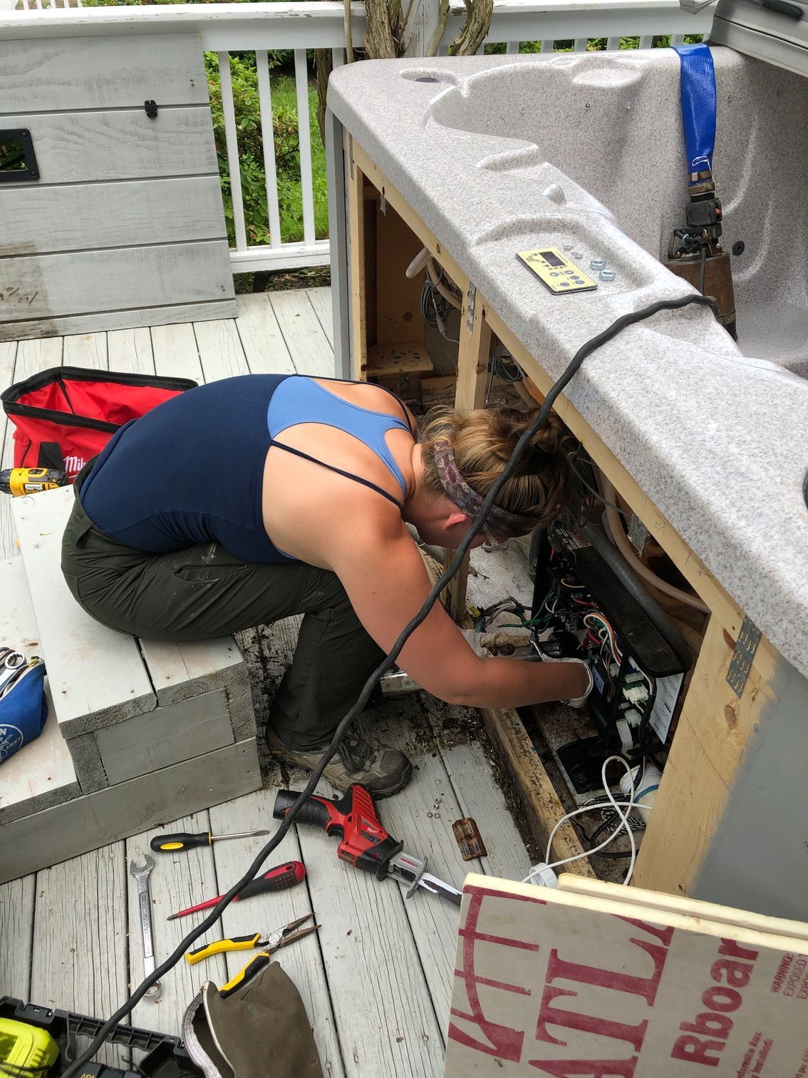 Woman repairs hot tub on wooden deck, reaching inside the exposed frame.