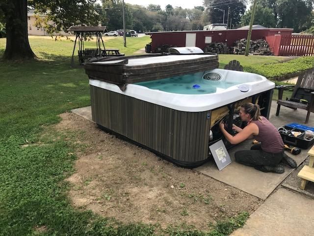 Woman working on hot tub, outdoor setting. Gray panels, blue water.