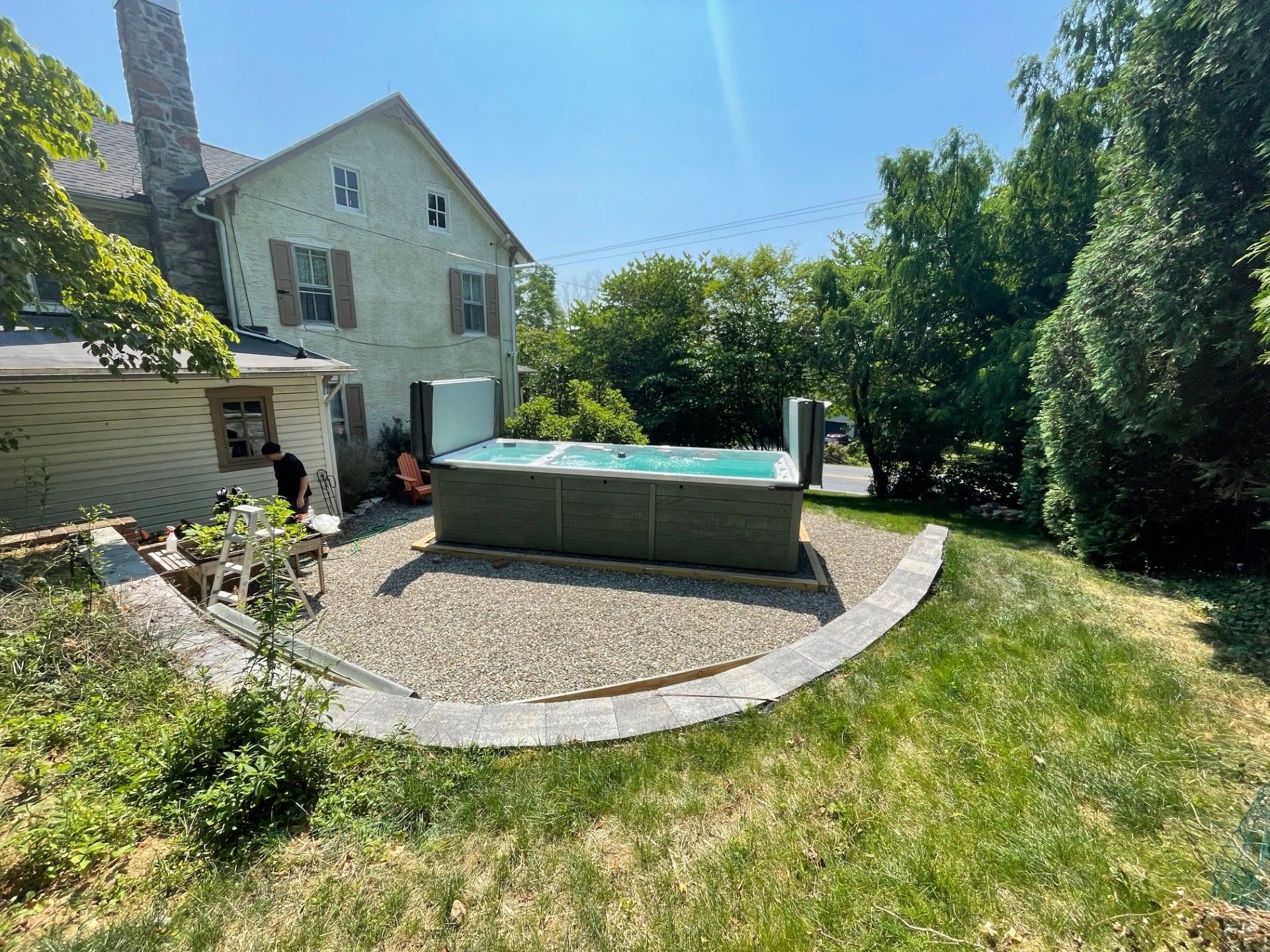 A backyard with a spa next to a house with stone and beige exterior; sunny day.