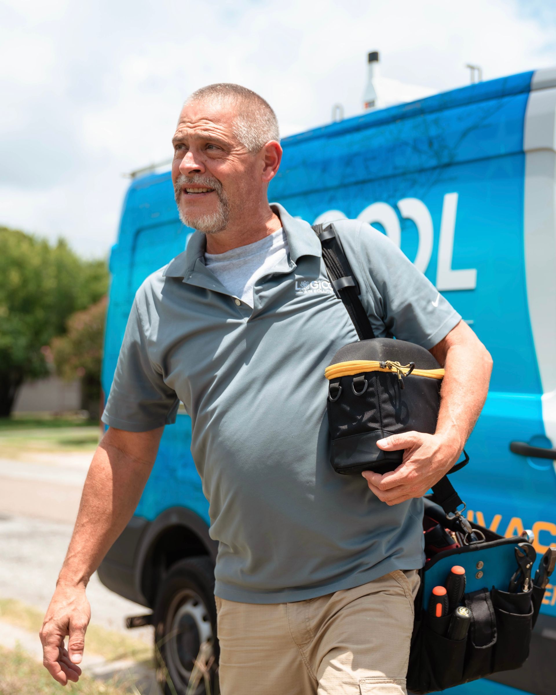 Man walking outdoors beside a blue van, carrying tools and a black bag