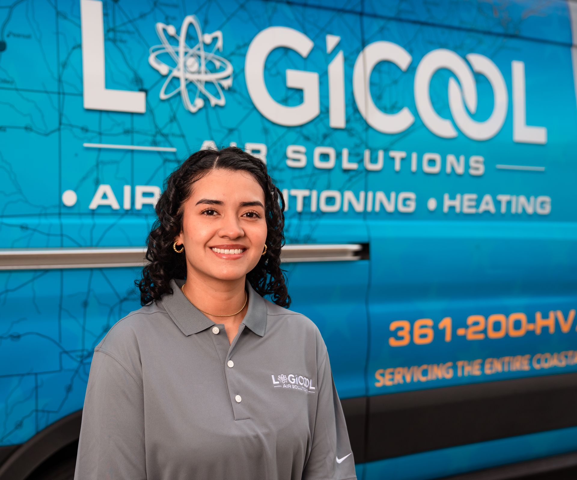 Woman in gray polo standing in front of a blue Logicool HVAC service van and smiling