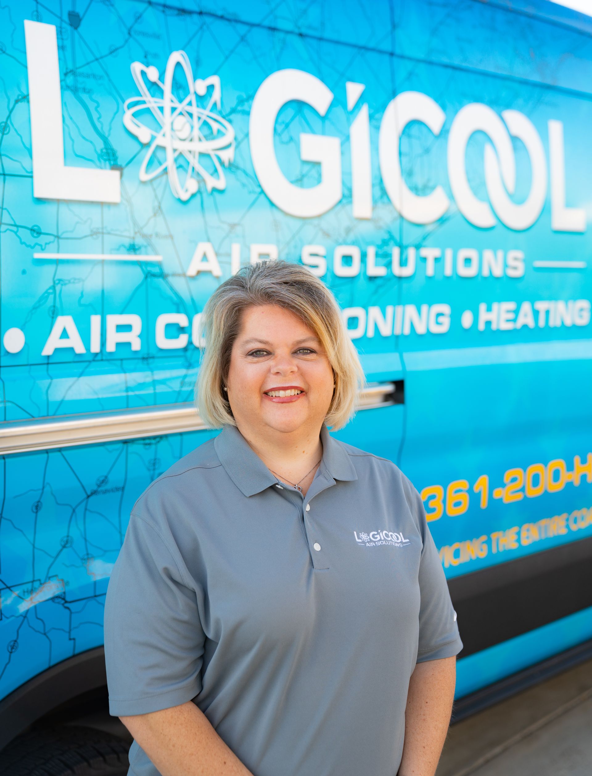 Woman in a gray polo standing in front of a blue LGICOL Air Solutions service van.