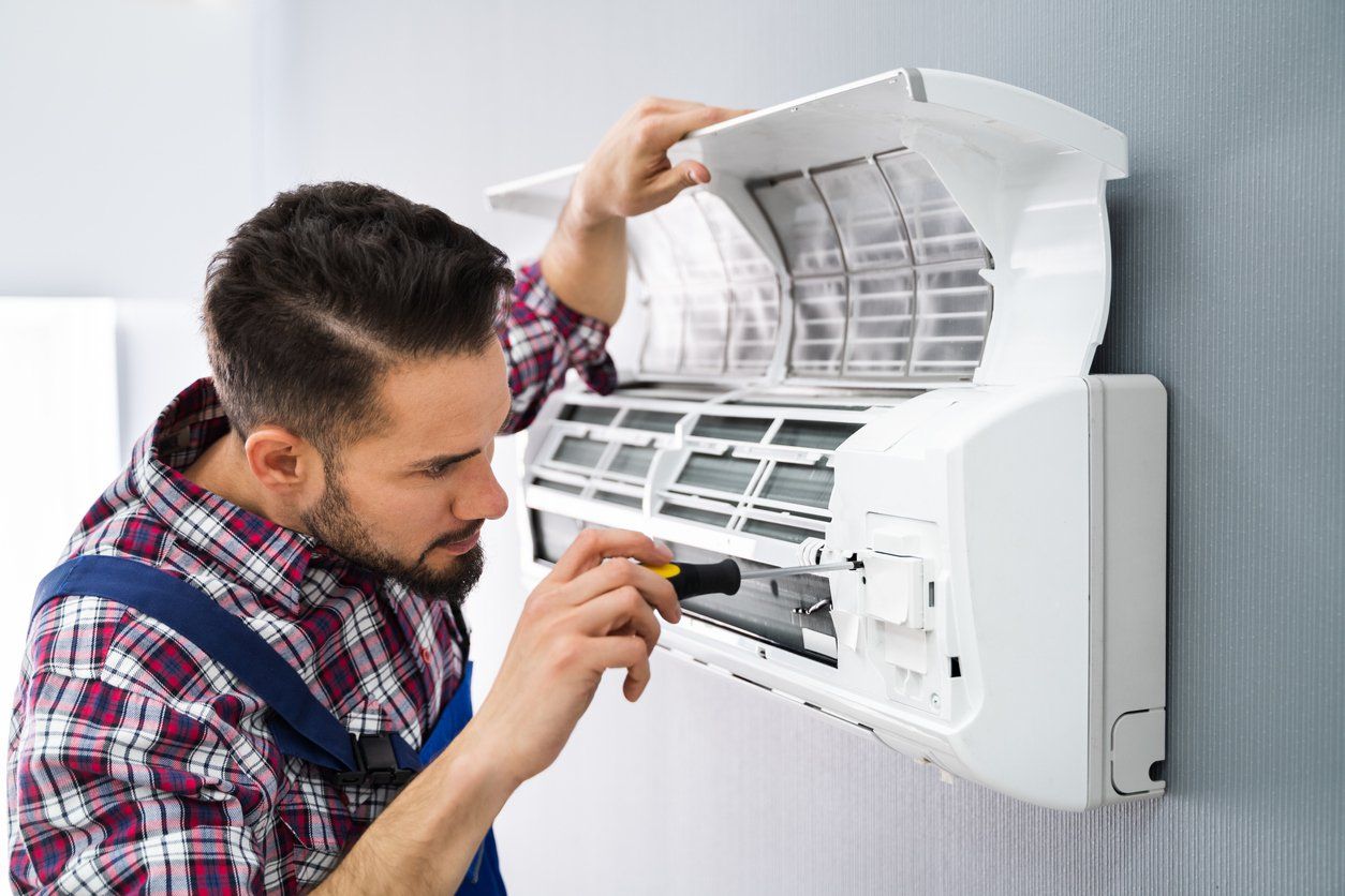 Technician repairing a wall-mounted air conditioner with the front panel open