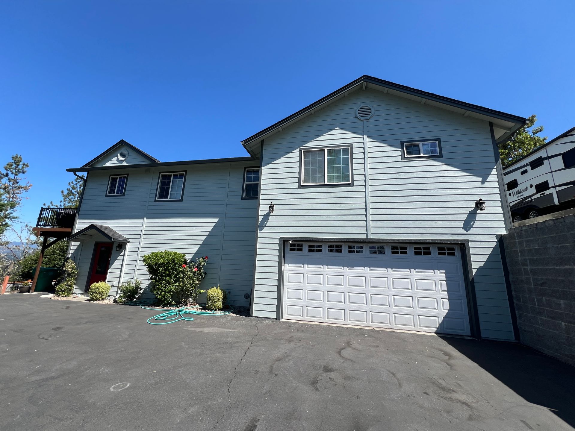 Two-story, light blue house with a white garage door on a paved lot under a blue sky.
