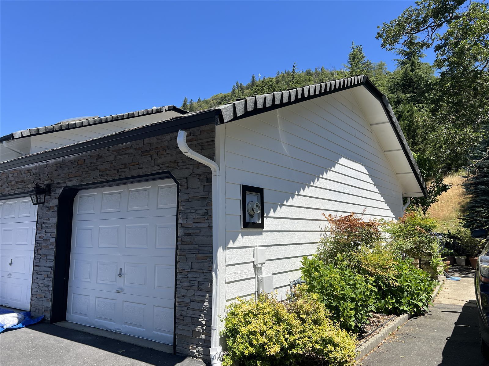Garage side gable with stacked-stone wainscot below white siding and black fascia
