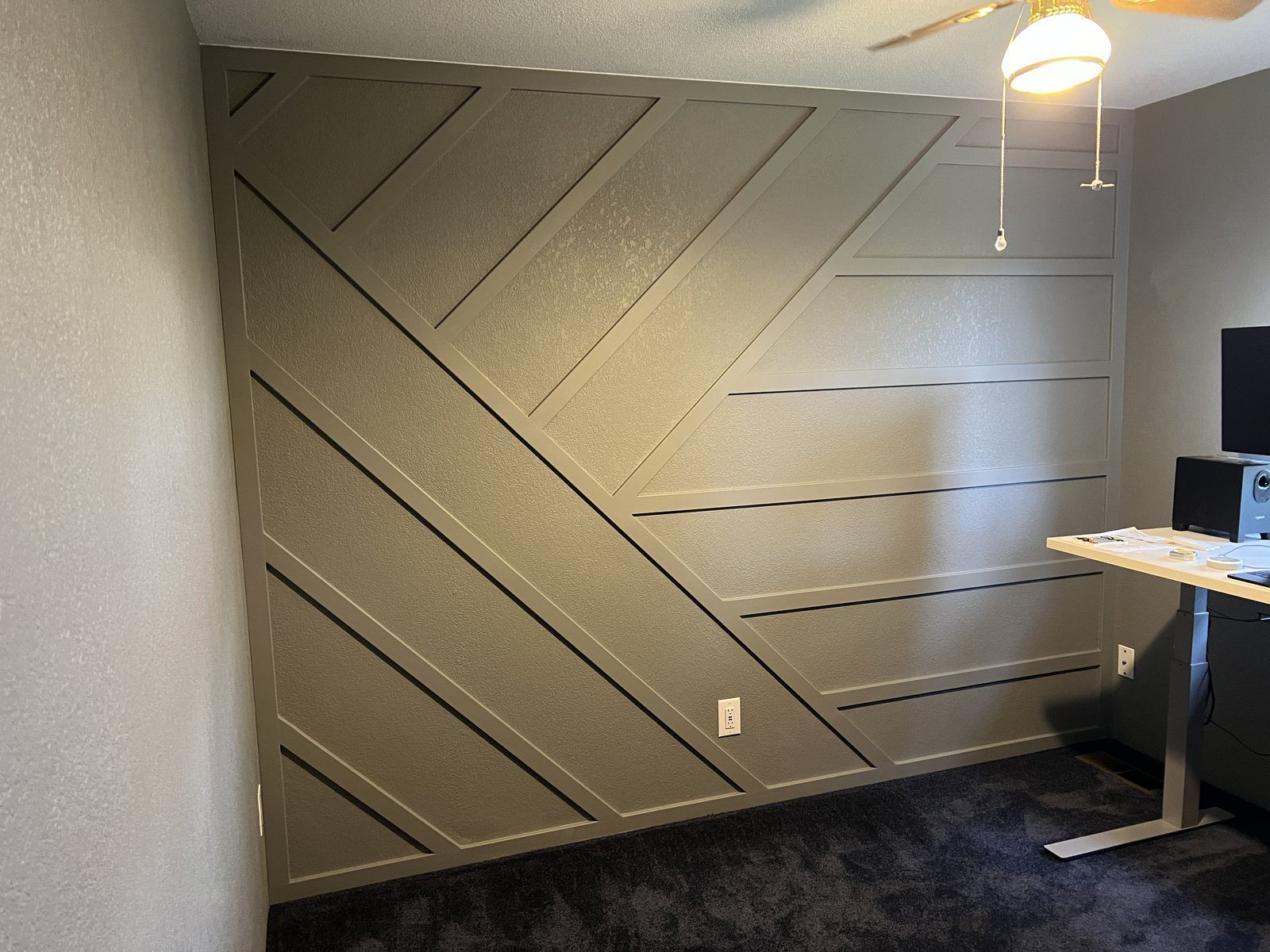 Gray geometric accent wall with raised trim beside a window.