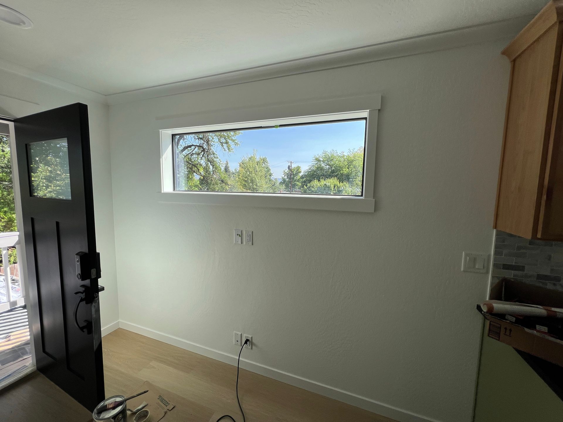 Interior room with white walls, a window overlooking trees, a black door, and a wooden floor.