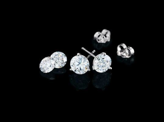 A pair of diamond stud earrings on a black surface.