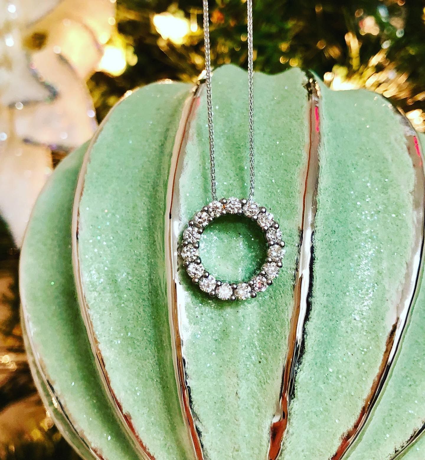Green Christmas ornament with a rhinestone ring pendant hanging in front of a blurred tree background