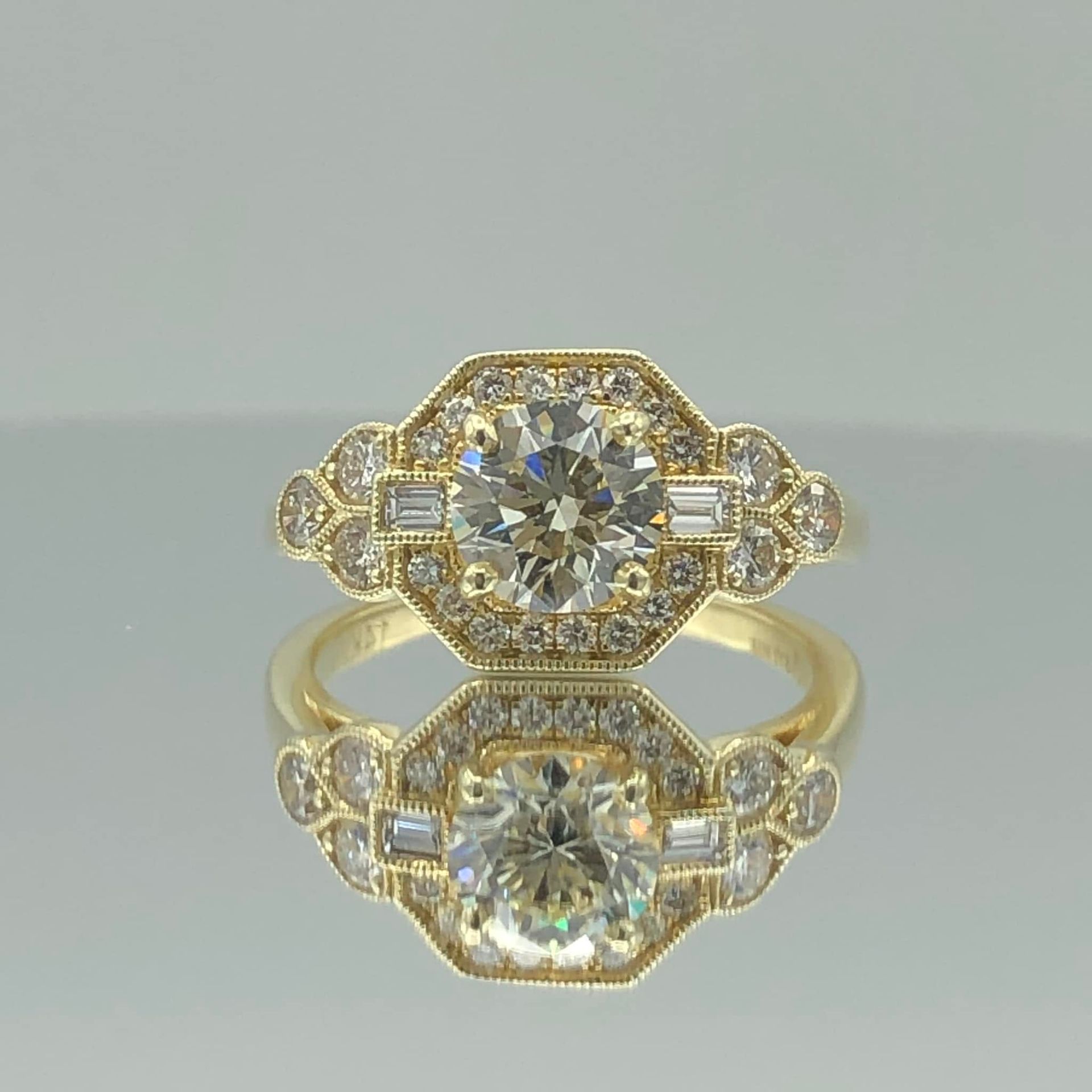 Gold ring with a round diamond and halo setting, shown with its reflection on a glossy surface