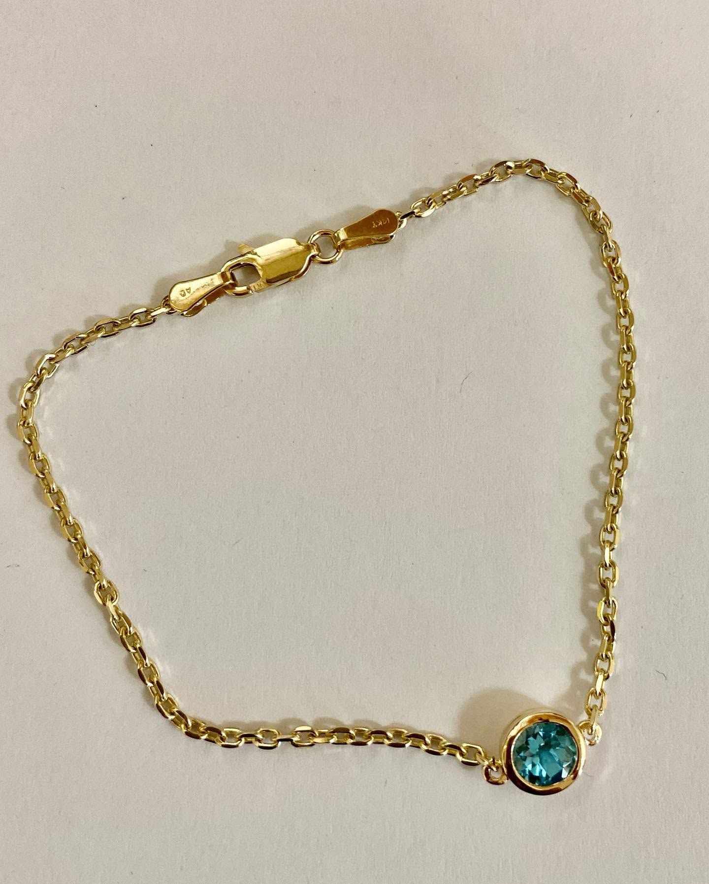 Gold chain bracelet with a turquoise round charm on a white background