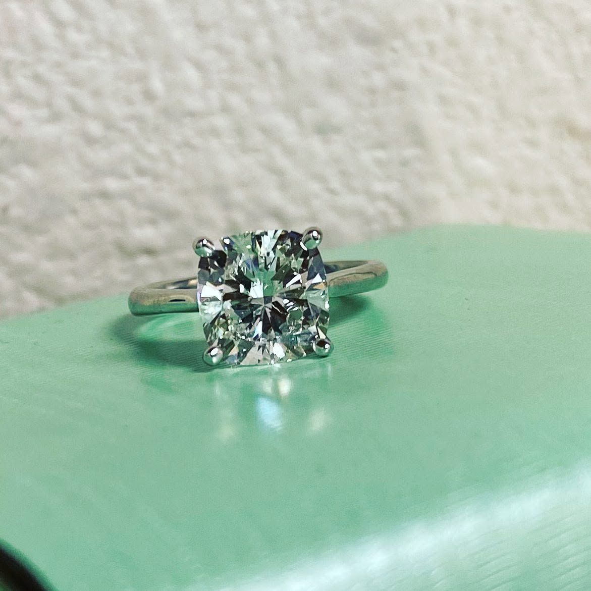 Silver ring with a square-cut green gemstone on a mint-green surface