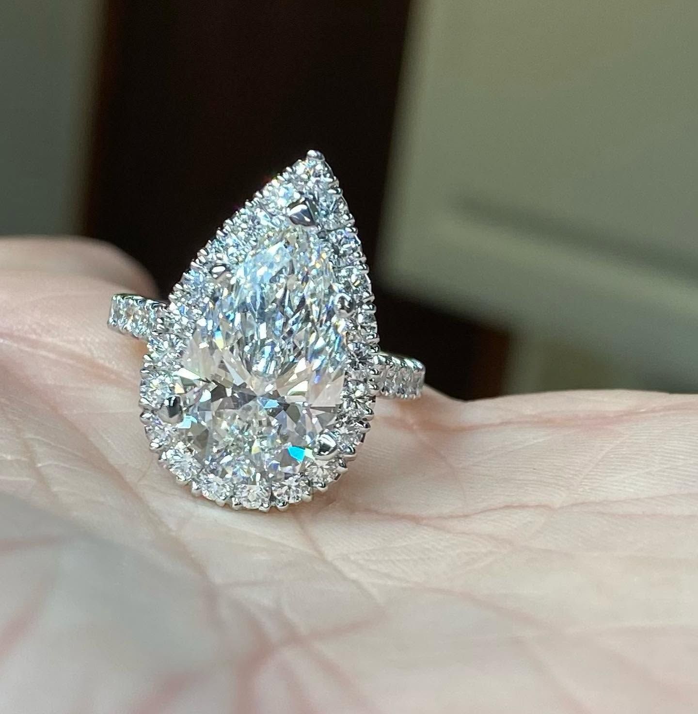 Teardrop-shaped diamond ring on a hand, with a halo of small sparkling stones.