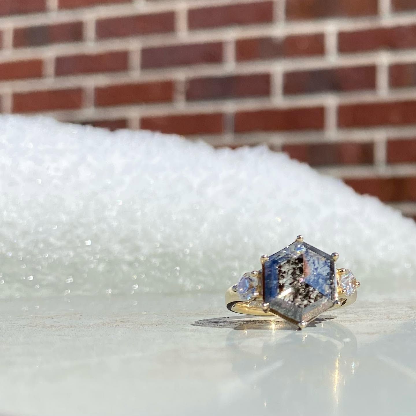 Hexagonal gemstone ring with blue stones on a white surface, against a brick wall and snowy background