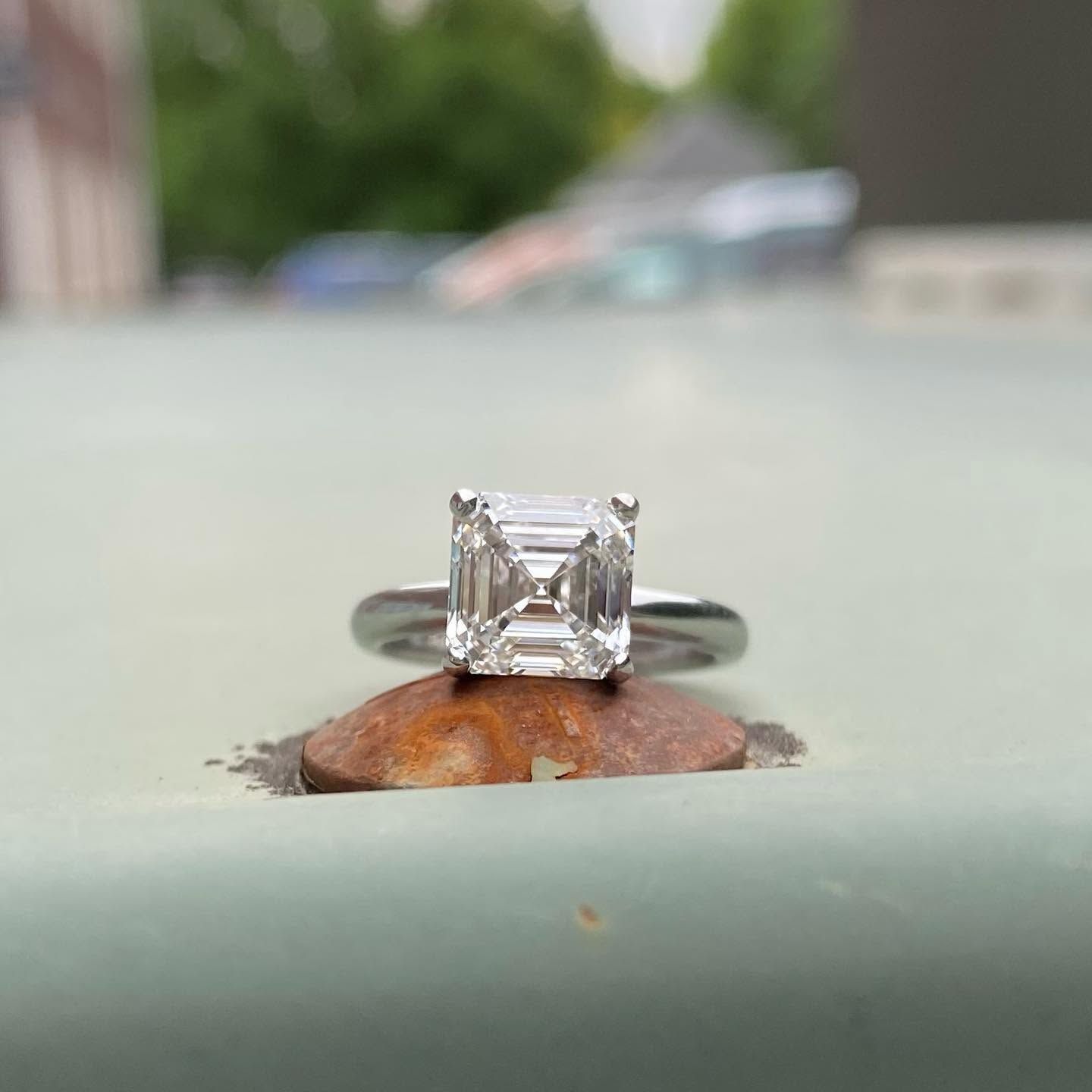 Clear square-cut diamond ring on a leaf, with a blurred outdoor background