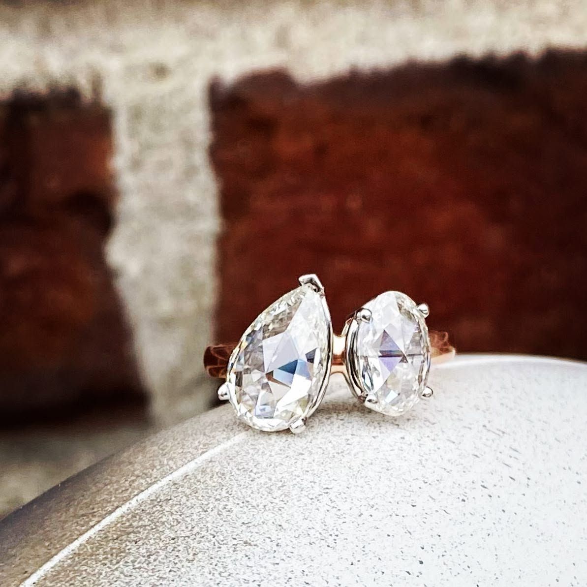 Pair of clear teardrop-cut stud earrings on a white surface, with a blurred brick background