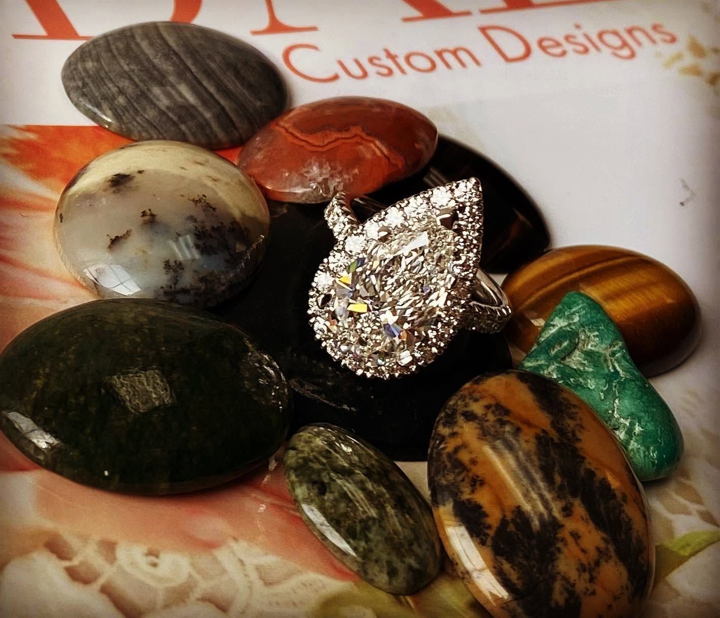 Assorted polished gemstone cabochons and a diamond ring on a Custom Designs display card