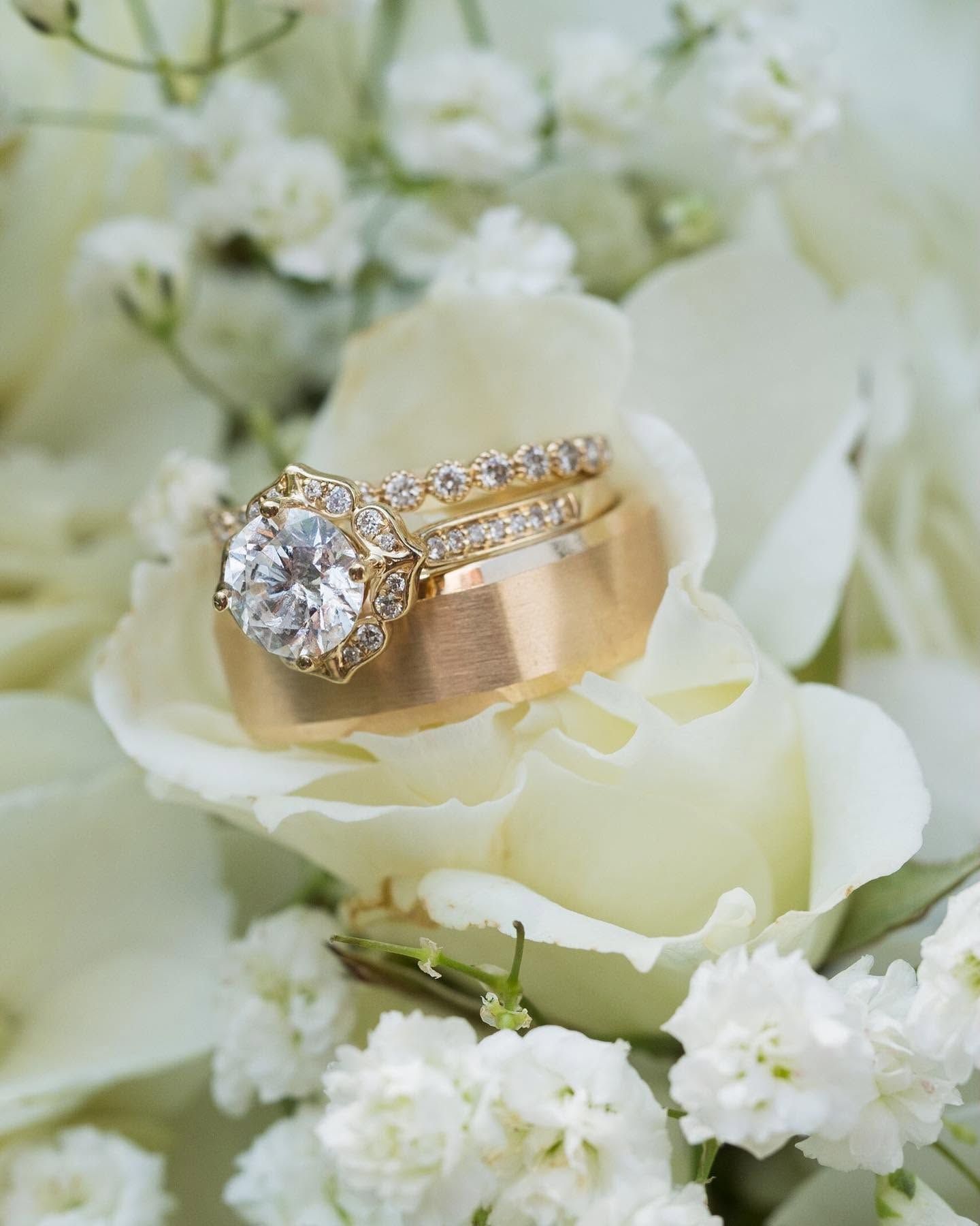 Gold and diamond engagement rings resting on a white rose with soft white flowers around them