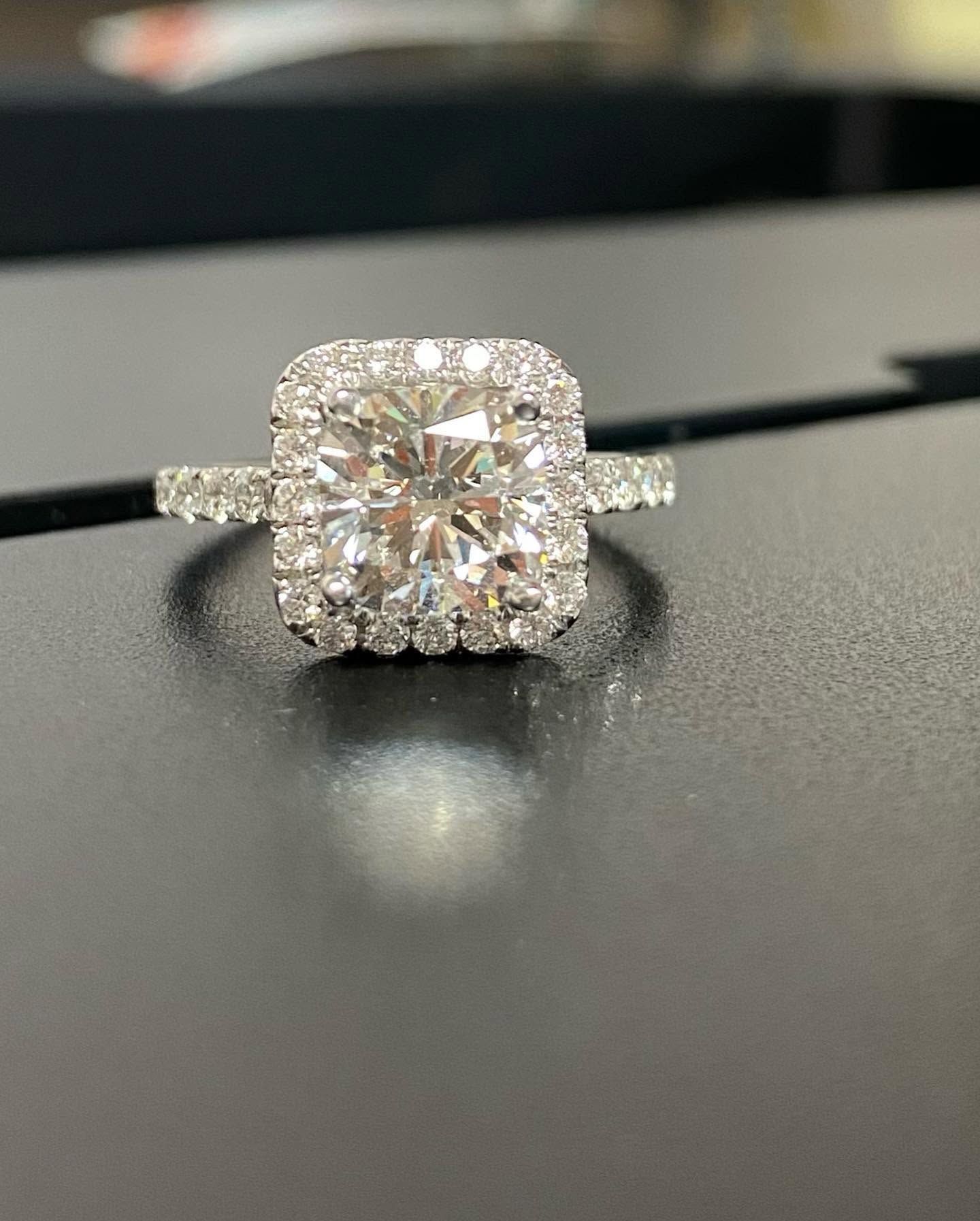 Diamond engagement ring on a black surface, featuring a round center stone with a halo setting.
