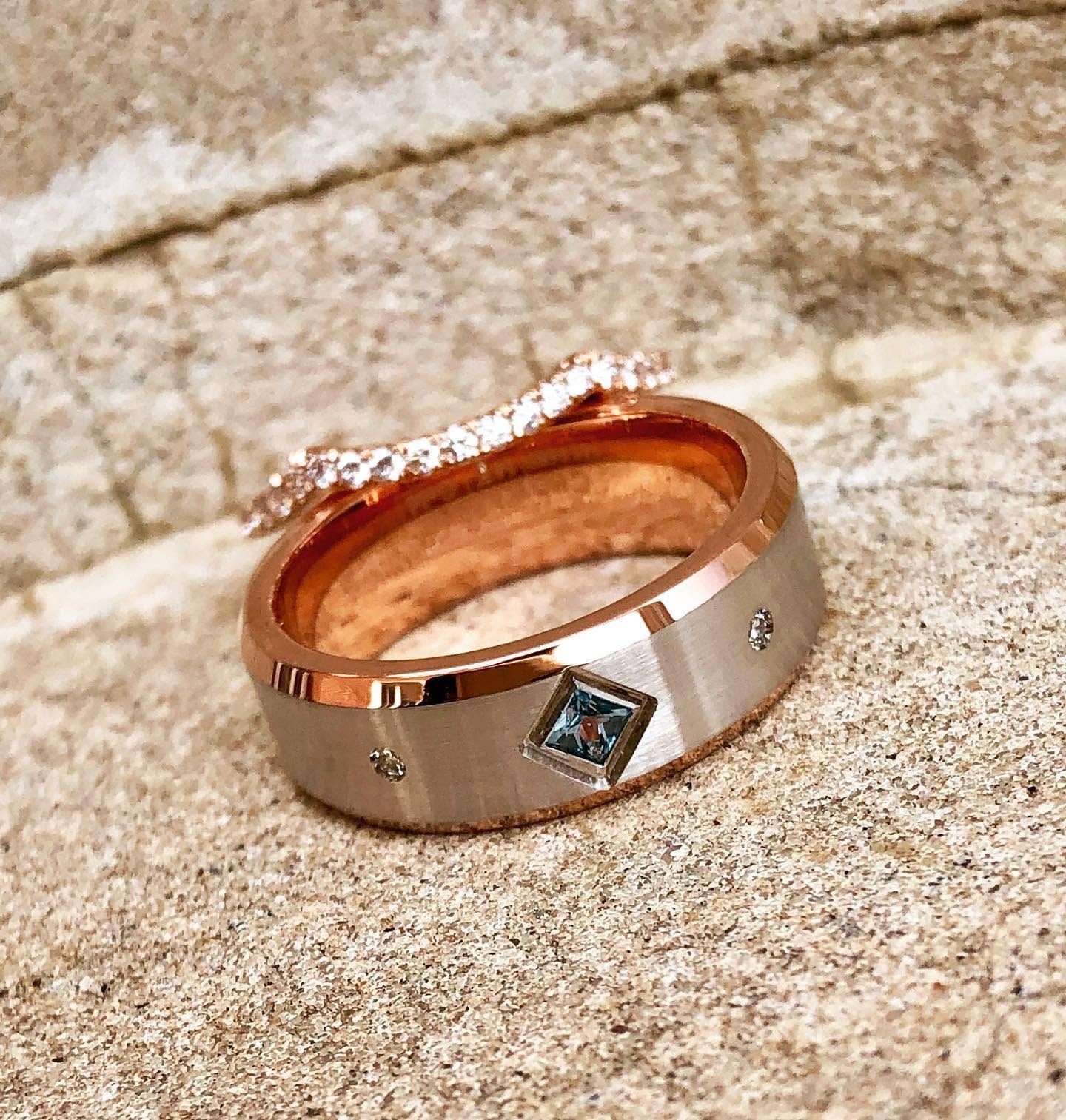 Rose-gold ring with small blue and clear stones resting on a textured stone surface