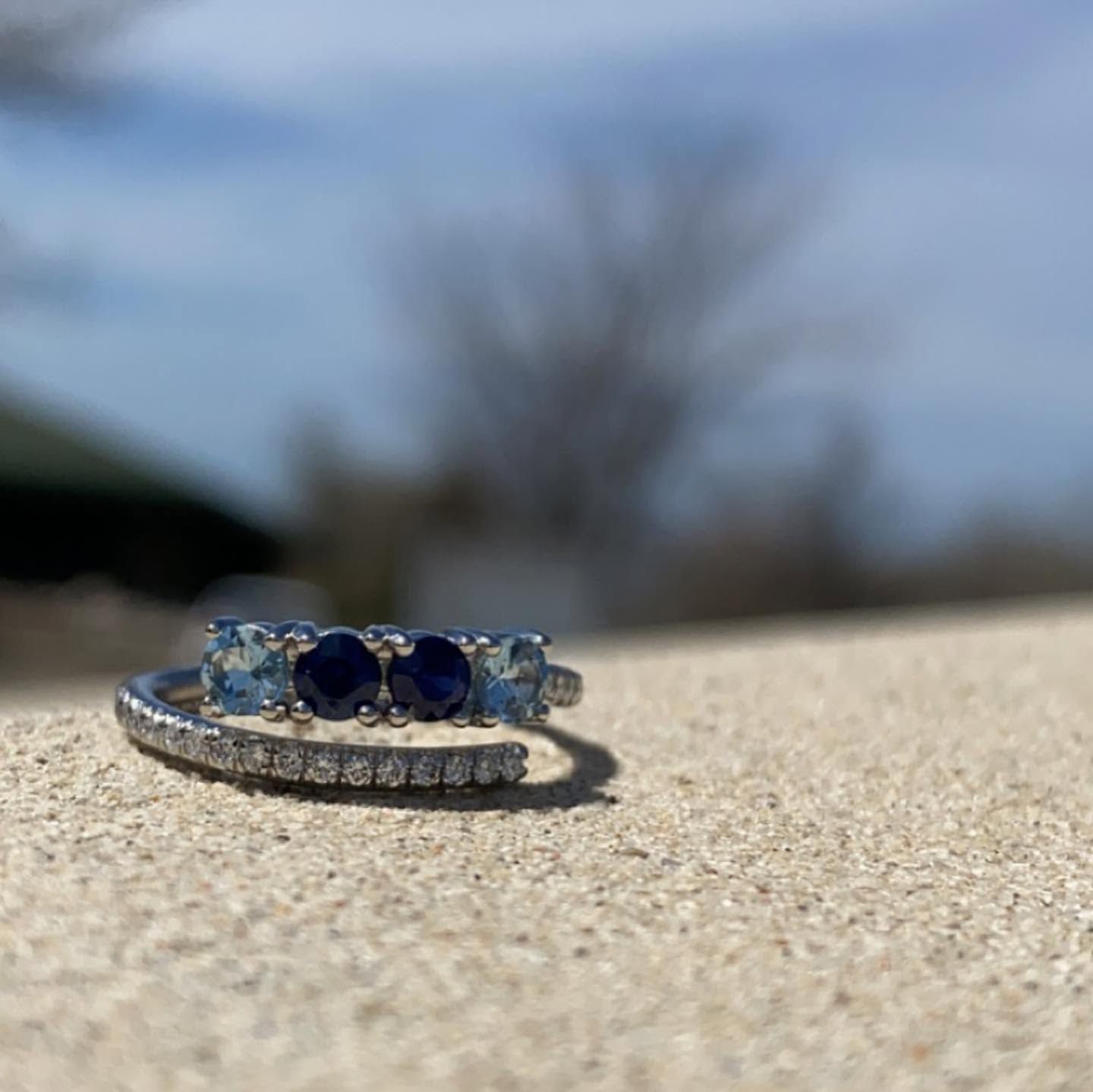 Blue gemstone ring on a beige surface, with a blurred outdoor background